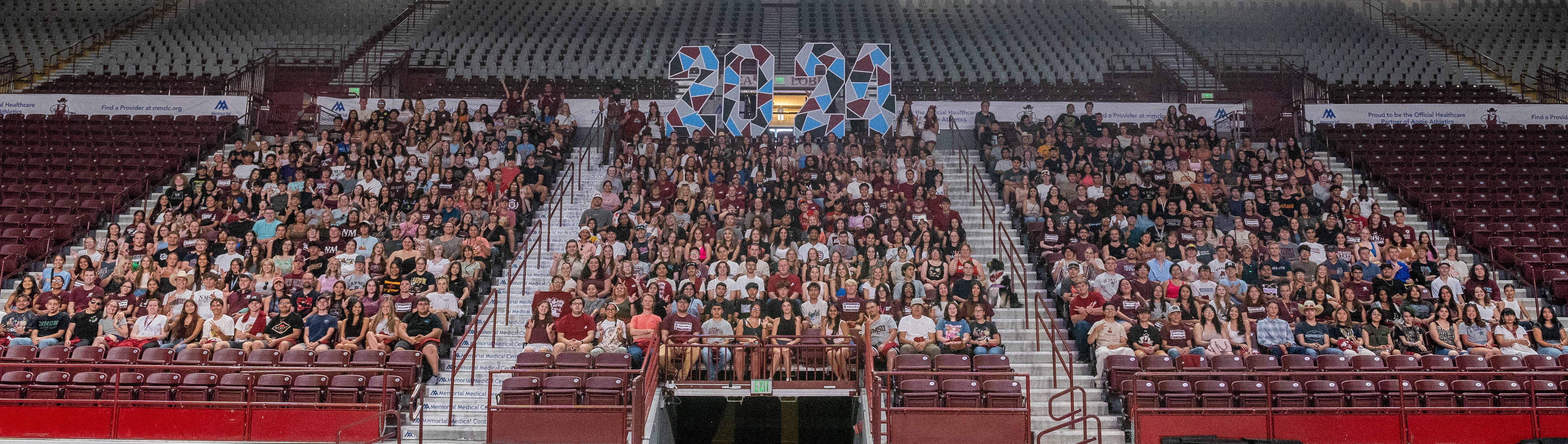 A large group of students seated in a sports arena, gathered for an event or orientation.